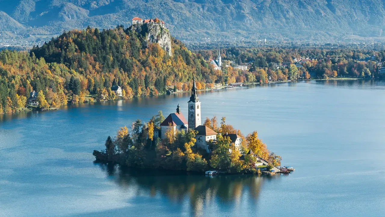Le lac de Bled avec son église sur l'île et son château au sommet de la falaise, entouré de forêts d'automne et des Alpes juliennes saupoudrées de neige, en Slovénie